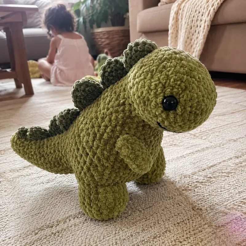 Dinosaurio de crochet verde musgo en el suelo de la sala.